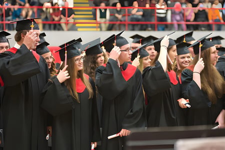 Eine Gruppe von Absolventinnen und Absolventen der Lambton Central Collegiate & Vocational School steht in schwarzen Talaren vor einer bunten Wand mit Flaggen.