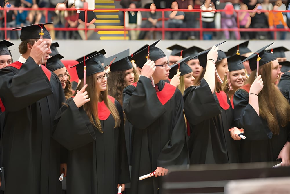 Eine Gruppe von Absolventinnen und Absolventen der Lambton Central Collegiate & Vocational School steht in schwarzen Talaren vor einer bunten Wand mit Flaggen.