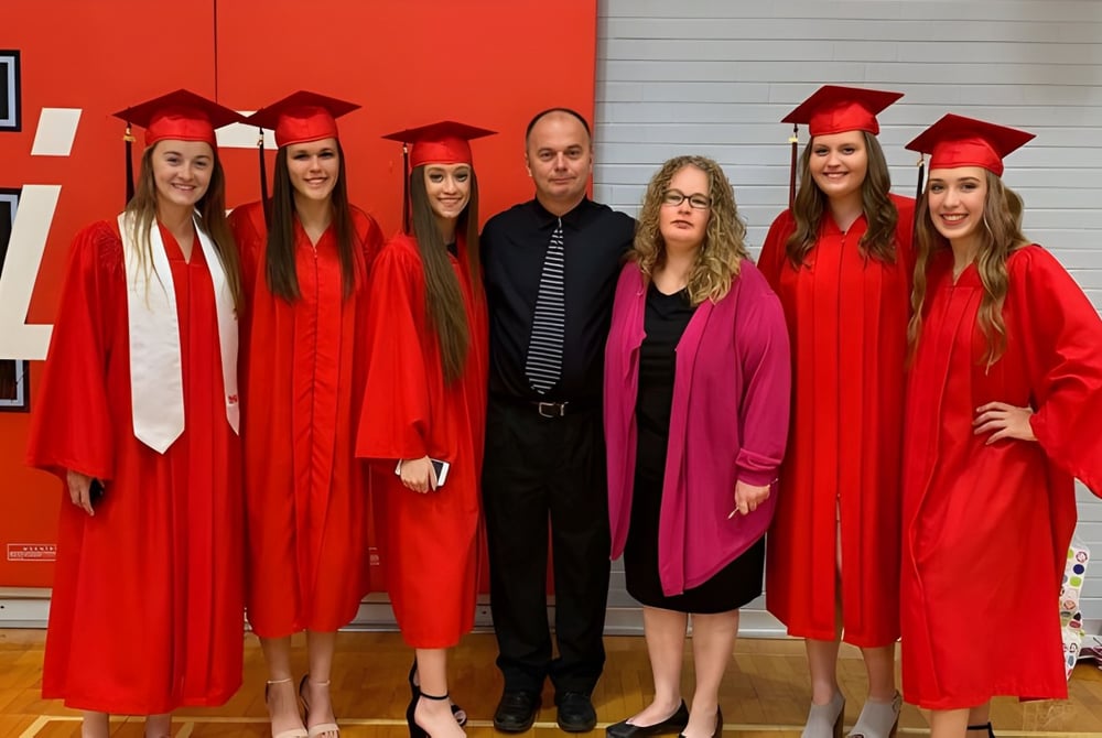 Eine Gruppe von Schülern der Lambton Kent Composite School steht in roten Abschlussgewändern vor einer roten Wand.