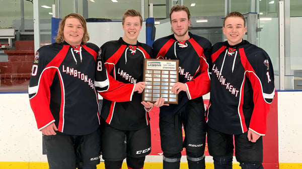 Vier Schüler in Hockeyuniformen halten eine Trophäe vor dem Hockeyfeld auf dem Campus der Lambton Kent Composite School.