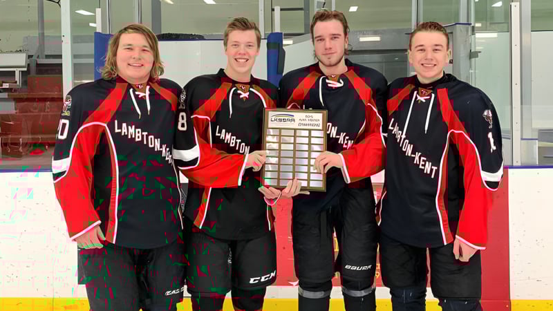 Vier Schüler in Hockeyuniformen halten eine Trophäe vor dem Hockeyfeld auf dem Campus der Lambton Kent Composite School.