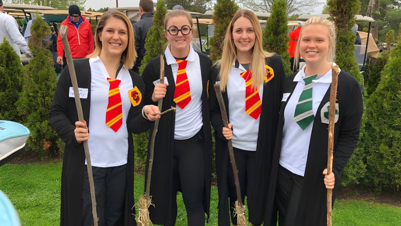 Vier Schülerinnen der Lambton Kent Composite School tragen Hogwartsartige Roben und Schals im Freien vor Baeumen und Gebaeuden.