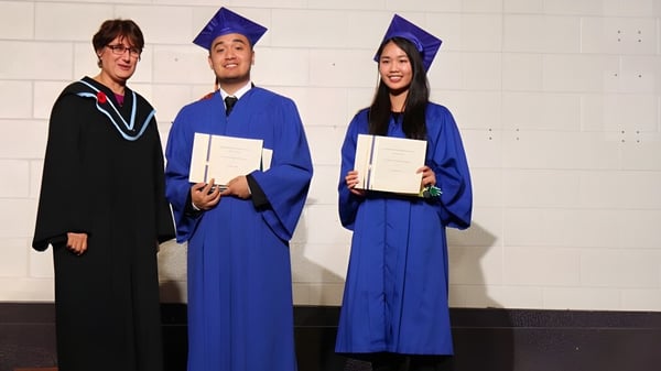 Drei Absolventinnen und Absolventen des L'Amoreaux Collegiate Institute stehen mit ihren Diplomen vor einer weißen Wand.