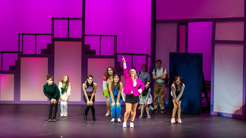 Eine Gruppe von Schülerinnen und Schülern der Lancaster Country Day School steht auf einer Bühne vor einem farbenfrohen lila und rosa Hintergrund mit geometrischen Mustern.