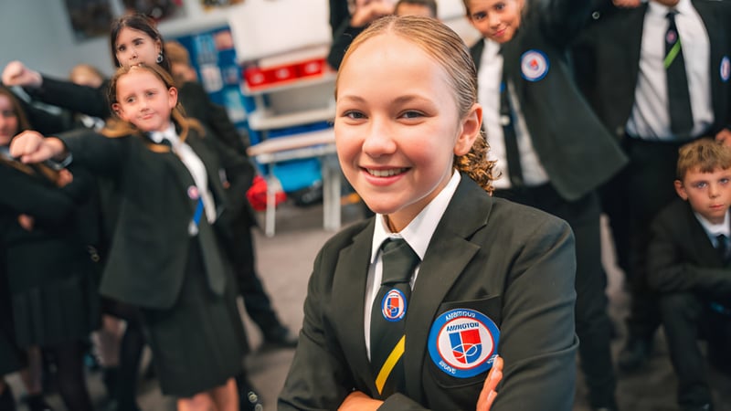 Eine Schülerin der Landau Forte Academy Amington steht im Vordergrund, im Hintergrund sind Personen in formeller Kleidung zu sehen.