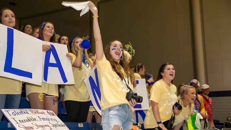 Eine Gruppe von Schülerinnen und Schülern der Lander University trägt gelbe Shirts und jubelt bei einer Sportveranstaltung.