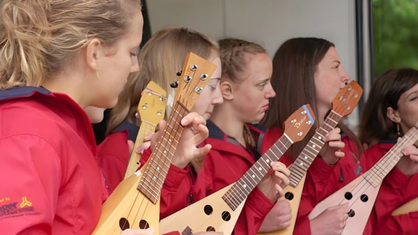 Eine Gruppe Schüler der Langley Fine Arts School steht in roten Uniformen mit verschiedenen Gitarren in einem Probenraum.