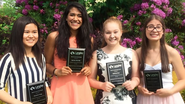 Vier Schülerinnen der Langley Fine Arts School stehen zusammen in einem Garten mit pinken Blumen im Hintergrund.