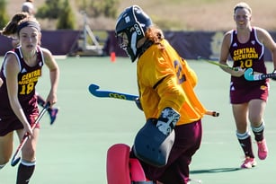 Schüler der Langley School spielen Feldhockey auf dem Sportplatz mit einem Spieler in gelber Uniform im Vordergrund.