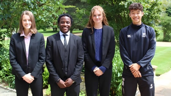 Vier Personen in formeller Kleidung stehen gemeinsam im Grünen auf dem Campus der Langley School.
