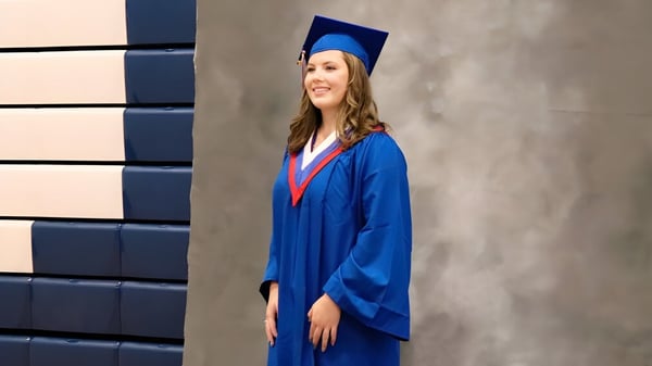 Eine Absolventin in blauer Robe steht vor einer grauen Wand auf dem Campus der Langley Secondary School.