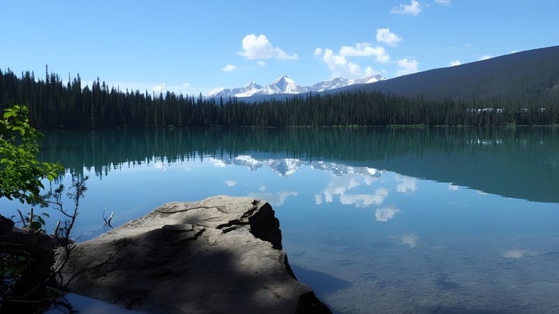 Ein klarer Bergsee mit Spiegelung der schneebedeckten Gipfel vor dem Hintergrund der Langley Secondary School.