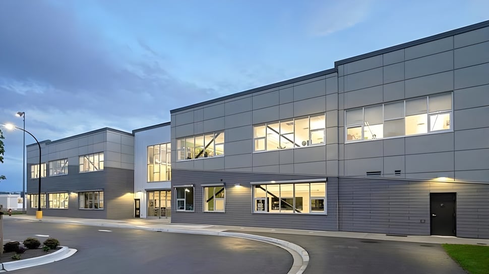 Das moderne mehrstöckige Schulgebäude der Langley Secondary School mit großen Fenstern und einer gebogenen Auffahrt bei bewölktem Himmel.