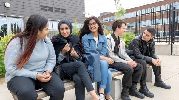 Schüler sitzen auf einer Bank vor einem modern gestalteten Gebäude auf dem Campus der Langley Secondary School.