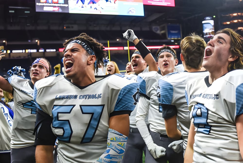 Schüler der Lansing Catholic High School feiern gemeinsam auf dem Fußballfeld vor der Anzeigetafel und Stadionbeleuchtung.