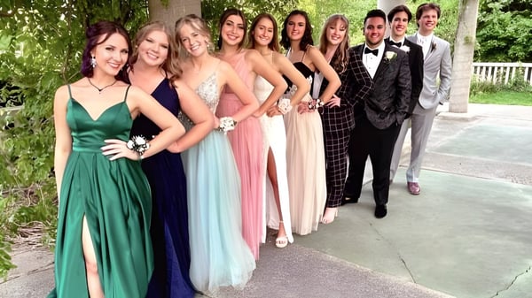 Eine Gruppe elegant gekleideter Personen steht gemeinsam im grünen Außenbereich der Lansing Catholic High School.