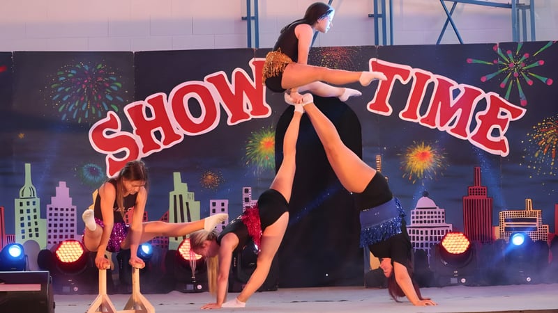 Eine Gruppe von Performerinnen und Performern steht auf der Bühne mit dem Schriftzug Show Time im Hintergrund auf dem Campus des Largy College.