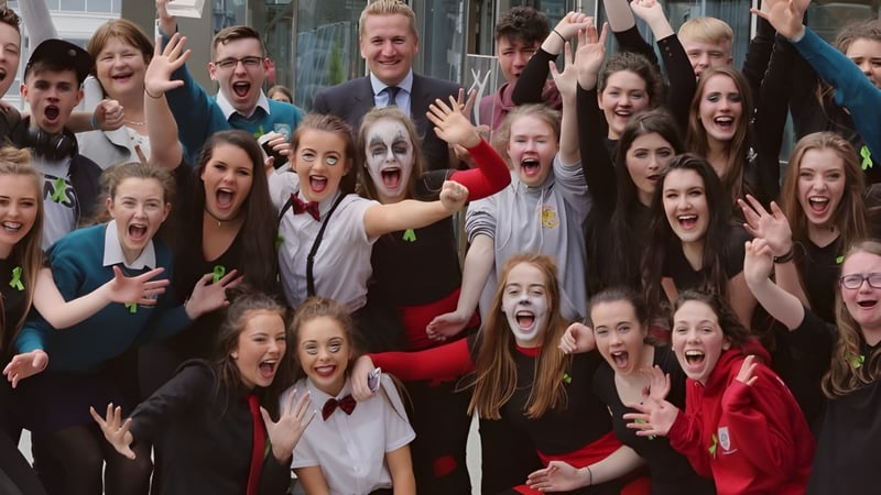 Eine Gruppe von Schülerinnen und Schülern beim Feiern mit erhobenen Händen auf dem Campus des Largy College, begleitet von einem Mann im Anzug.