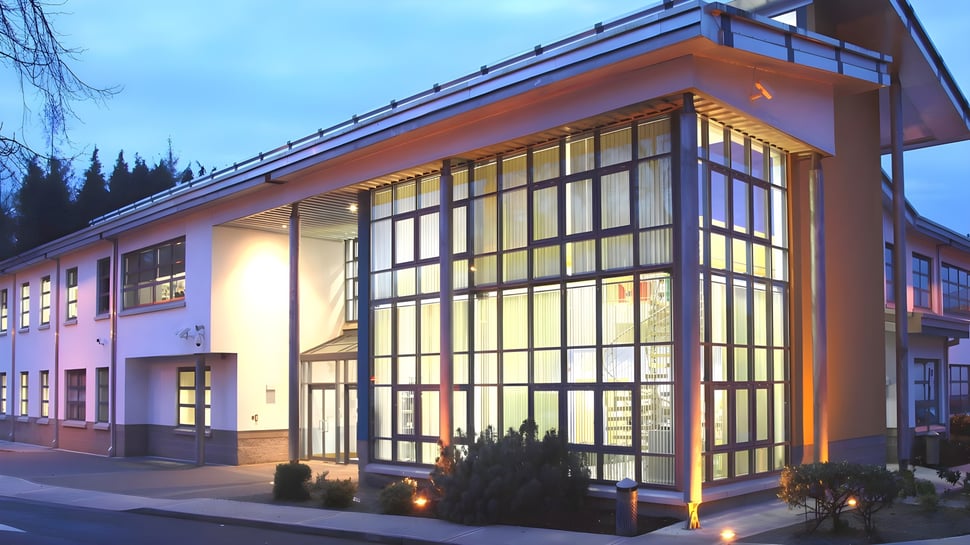 Das modern gestaltete Gebäude mit Glasfassade und schrägem Dach von Largy College steht in einem bewaldeten Gebiet und ist abends beleuchtet.