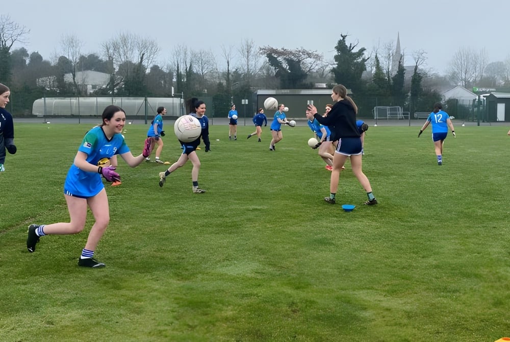 Eine Gruppe von Schülerinnen und Schülern des Largy College spielt ein Spiel auf einem Rasenplatz mit Bäumen und Gebäuden im Hintergrund.
