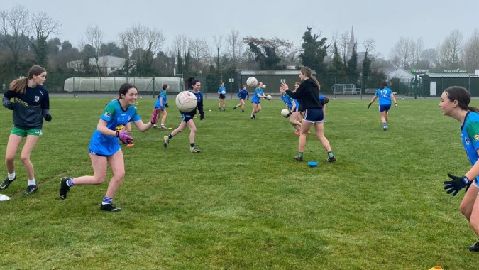 Schülerinnen und Schüler des Largy College spielen ein Spiel auf dem Sportfeld mit Bäumen und Gebäuden im Hintergrund.