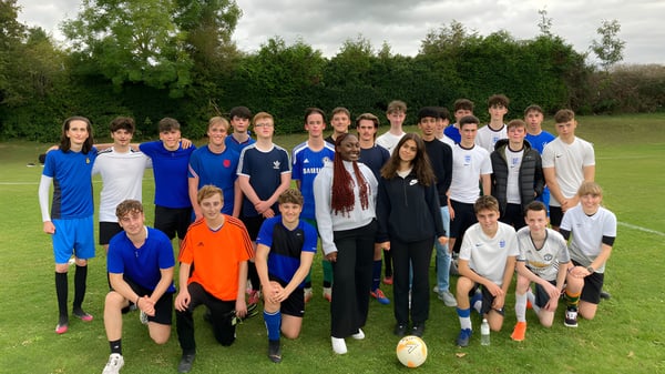 Eine Gruppe Schülerinnen und Schüler steht auf einer Wiese mit Bäumen im Hintergrund auf dem Gelände der Larkmead School.