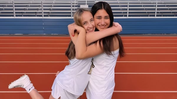 Zwei Schülerinnen des Las Virgenes Unified School District umarmen sich auf einer roten Laufbahn vor Stadionrängen.
