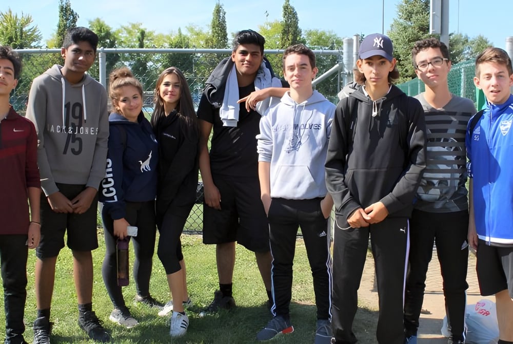 Eine Gruppe von Schülerinnen und Schülern steht auf einem Grünfeld vor Gebäuden auf dem Campus der LaSalle Community Comprehensive High School.