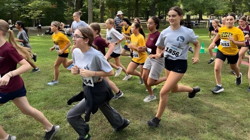 Eine Gruppe von Schülerinnen und Schülern der LaSalle Community Comprehensive High School nimmt an einem Laufwettbewerb auf einem grasbewachsenen Feld teil.