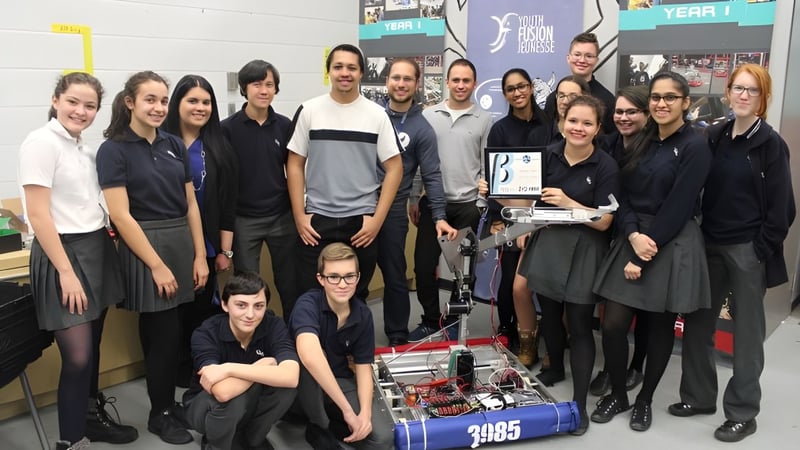 Eine Gruppe Schüler posiert in einem Workshopraum der LaSalle Community Comprehensive High School mit verschiedenen Geräten im Hintergrund.
