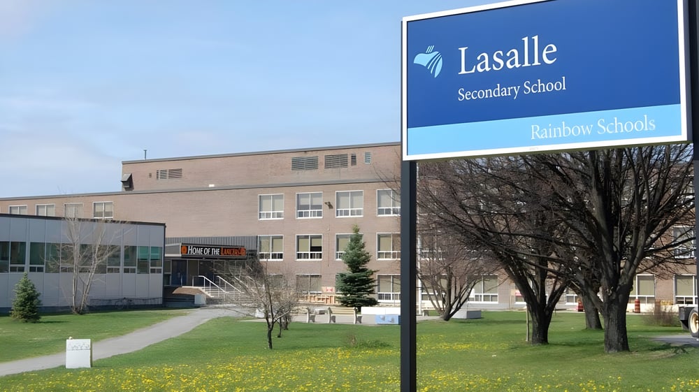 Das Gebäude der La Salle Secondary School mit Schulnamen und Logo ist von Bäumen und einer Rasenfläche umgeben.