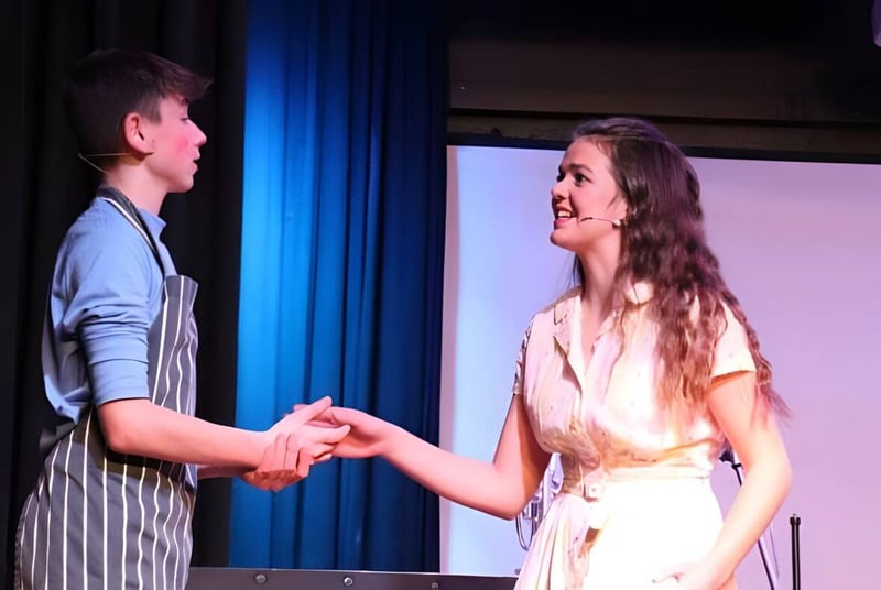 Zwei Personen stehen auf einer Bühne der Lathallan School und geben sich die Hand vor einem blauen Vorhang.
