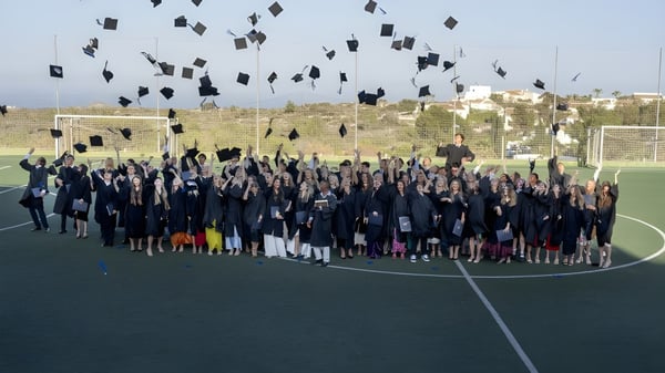 Eine große Gruppe von Absolventinnen und Absolventen der Laude Lady Elizabeth School wirft ihre Abschlussmützen auf dem Sportplatz in die Luft.