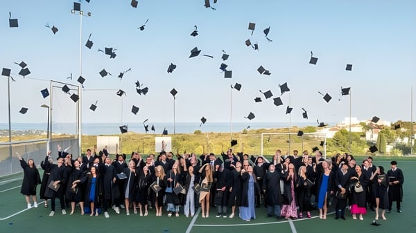 Schülerinnen und Schüler der Laude Lady Elizabeth School feiern ihre Abschlussfeier auf dem Sportfeld und werfen ihre Hüte in die Luft.
