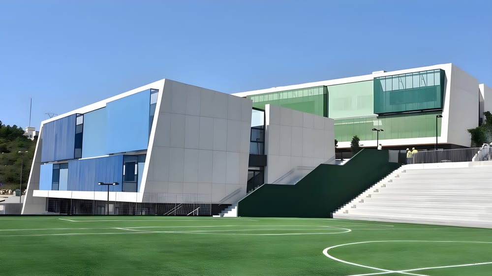 Das moderne Gebäude der Laude Lady Elizabeth School mit einem grünen Sportplatz im Vordergrund unter klarem Himmel.