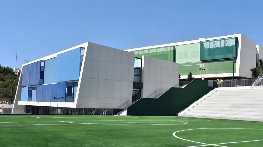 Das moderne mehrfarbige Gebäude der Laude Lady Elizabeth School mit grünem Rasen und Fußballfeld im Vordergrund.