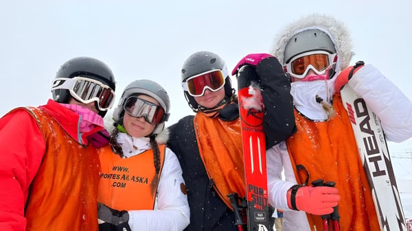 Eine Gruppe von Skifahrern in bunter Winterkleidung steht vor verschneiter Kulisse auf dem Gelände der Laude Lady Elizabeth School.