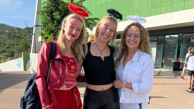 Drei Schülerinnen der Laude Lady Elizabeth School stehen in bunten Outfits vor einem grünen Gebäude.