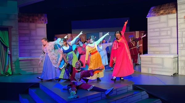 Eine Gruppe bunt gekleideter Darsteller steht auf der Bühne der Laurel School vor einem architektonischen Bühnenbild mit lebhafter Beleuchtung.