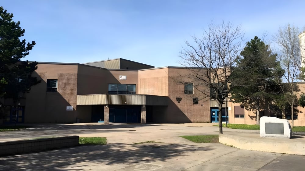 Das moderne Backsteingebäude mit Glaseingang der Laurier MacDonald High School ist von Bäumen und einem gepflasterten Bereich umgeben.