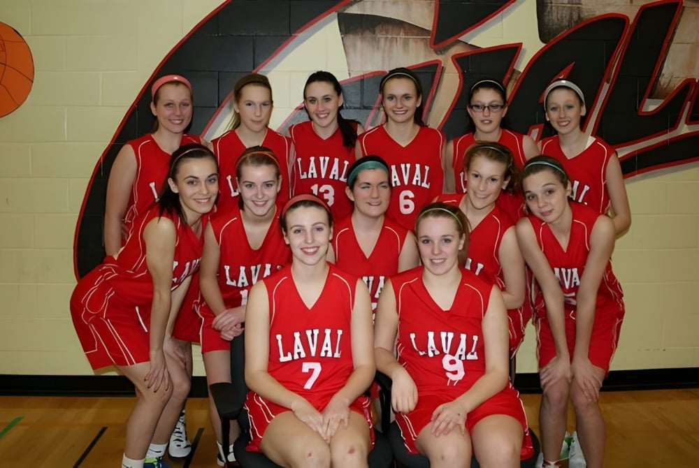 Eine Gruppe junger Schülerinnen der Laval High School in roten Uniformen posiert in der Sporthalle vor einem großen Basketball-Wandbild.