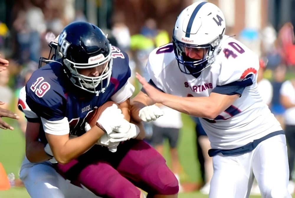 Zwei Footballspieler der Lawrence Academy führen einen Tackle auf dem Spielfeld während eines Spiels mit Zuschauern im Hintergrund aus.
