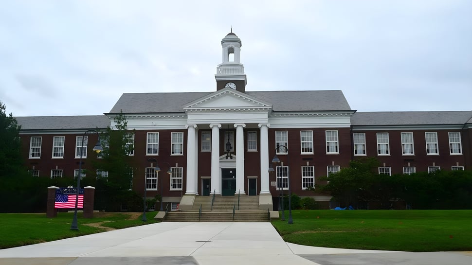 Das Backsteingebäude der Lawrence Academy mit zentralem Turm und Säulen steht auf einer Rasenfläche mit amerikanischer Flagge im Vordergrund.
