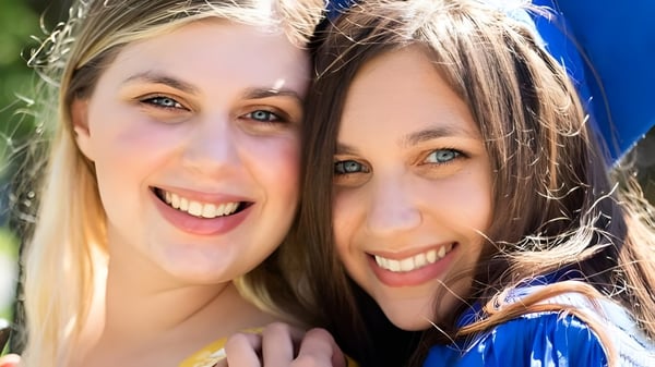 Zwei Schülerinnen der Lawrence Woodmere Academy umarmen sich im Freien vor einem grünen Hintergrund.