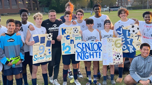 Eine Gruppe Schülerinnen und Schüler feiert Senior Night auf dem Rasen der Lawrence Woodmere Academy mit Schildern in den Händen.