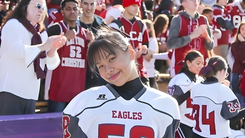 Eine junge Frau mit einem weißen Eagles-Trikot steht vor einer Gruppe von Menschen in roten Trikots auf dem Campus der Layton Christian Academy.