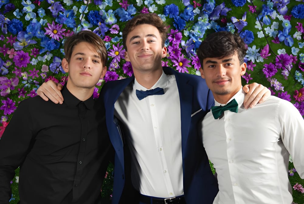 Drei Schüler der Layton Christian Academy posieren vor einem farbenfrohen Blumenhintergrund.