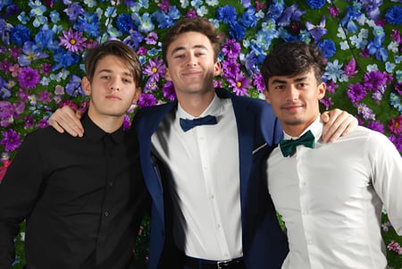 Drei Schüler der Layton Christian Academy posieren gemeinsam vor einem bunten Blumenhintergrund.