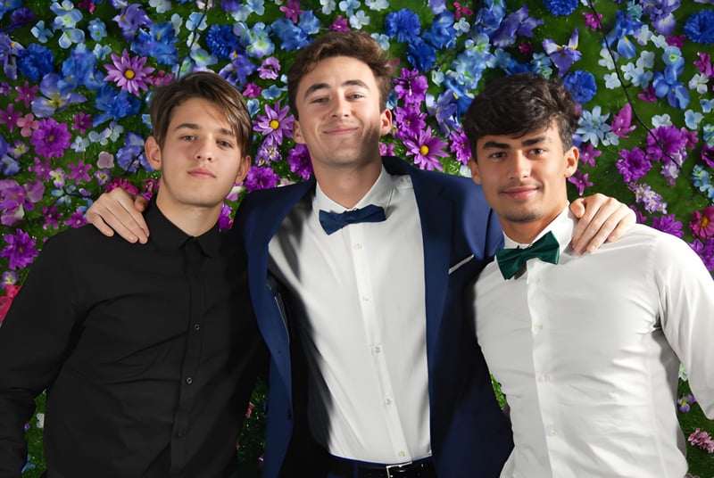 Drei Schüler der Layton Christian Academy posieren gemeinsam vor einem bunten Blumenhintergrund.