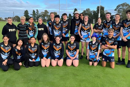 Eine Gruppe junger Athletinnen der Le Fevre High School posiert auf einem Rasenfeld vor Bäumen und blauem Himmel.